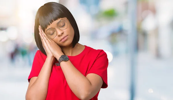 Beautiful young african american woman wearing glasses over isolated background sleeping tired dreaming and posing with hands together while smiling with closed eyes.