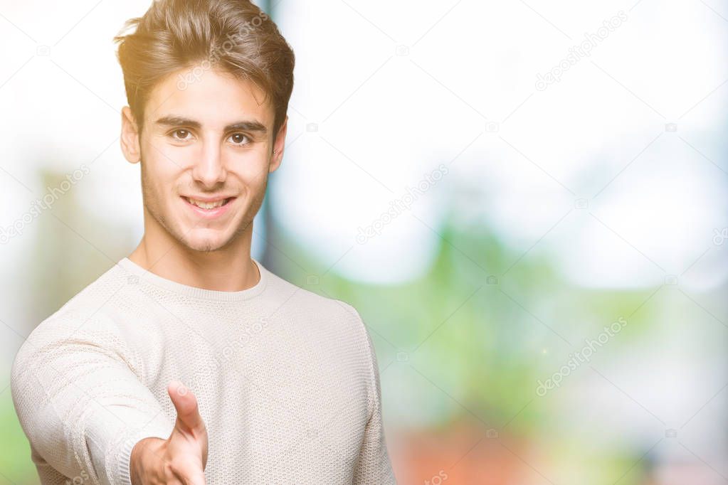 Young handsome man over isolated background smiling friendly offering handshake as greeting and welcoming. Successful business.