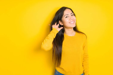Sarı izole arka plan üzerinde güzel esmer kadın kulak üzerinde el ile gülümseyen söylenti veya dedikodu bir işitme dinlerken. Sağırlık konsepti.