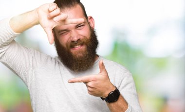 Genç Sarışın giyen sıradan kazak elle yapma çerçeve ve parmakları ile mutlu yüz gülümseyen adam. Yaratıcılık ve Fotoğrafçılık kavramı.