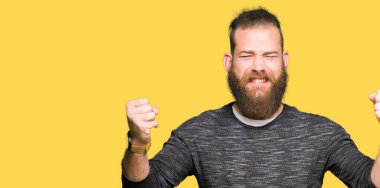 Gülümseyen ve başarı için çığlık rahat kazak çok mutlu ve heyecanlı kaldırdı, silah ile kazanan jest yapıyor giyen genç sarışın adam. Kutlama kavramı.