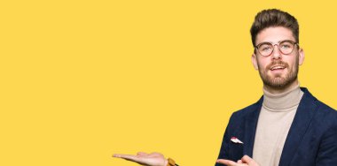 Hayret ve el ile sunulması ve parmak ile işaret ederken kameraya gülümseyen gözlüklü genç yakışıklı iş adamı.