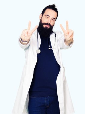 Doktor tıbbi ceket ve zafer işareti yapıyor parmak gösterilen kamera seyir gülümseyen stetoskop uzun saçlı. İki numaralı.