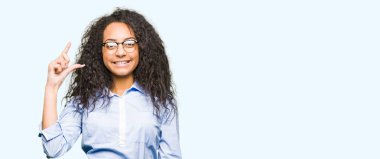 Kıvırcık saçlı Genç güzel iş kızı gözlük gülümseyen ve emin el ile boyutu işareti yaparken parmaklar ile görünümlü ve kamera bakıyor. Ölçü kavramı.