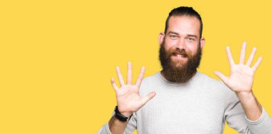 Genç sarışın adam rahat kazak gösteren ve parmak numarası on ile işaret giymiş iken emin ve mutlu gülümseyen.