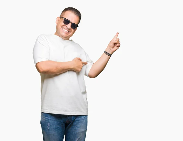 中年阿拉伯男子戴白色 T恤和太阳镜在孤立的背景与一个灿烂的微笑在脸上 用手和手指指着一边看着镜头 — 图库照片