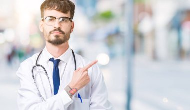 Genç doktor adam giyen hastane kat izole üzerinden reklam, ciddi ve sakin yüz gösterilen yan el parmak ile işaret arka plan