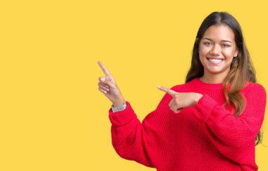 Gülümseyen ve iki elleri ve parmakları ile tarafına işaret kamera bakarak izole arka plan üzerinde kırmızı kış kazak giyen genç güzel esmer kadın.