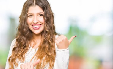 Beyaz kazak giyen genç güzel kadın kendinden emin gülümseyen arkasından el ve kadar başparmak ile işaret