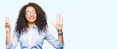 Kıvırcık saçlı gösterilen ve parmakları ile işaret gözlüklü genç güzel iş kız kendinden emin ve mutlu gülümseyerek süre yedi numara.