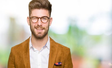 Seksi bir ifadeyle, neşeli ve mutlu yüzünü kameraya bakarak göz kırpıyor genç yakışıklı iş adam gözlük.