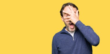 Orta yaş yakışıklı adam bir kazak giyen şok göz kaplayan yüz ve gözleri ile el, utanmış ifade ile parmaklar bakarak.