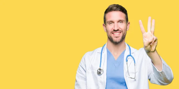 英俊的医生男子穿着医疗制服在孤立的背景显示和手指第三 同时微笑着自信和快乐 — 图库照片