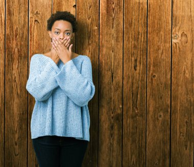 Üzerinde bir kazak giyen genç güzel Afrikalı-Amerikalı kadın arka plan ağız hata için elleriyle kapsayan şok izole. Gizli kavramı.