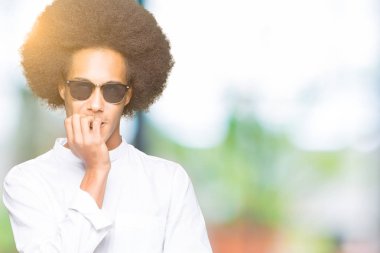 Afrikalı-Amerikalı genç afro saçlı stresli ve gergin elle çivi ısırma ağzına bakarak güneş gözlüğü takıyor. Anksiyete sorunu.
