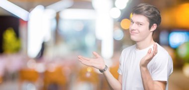 Üzerinde rahat beyaz t-shirt giyen genç yakışıklı adam arka plan clueless ve şaşkın bir ifadeyle kollar ve eller kaldırdı izole. Şüphe kavramı.