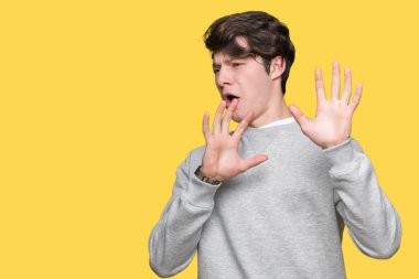 Üzerinde sweatshirt giyen genç yakışıklı sportif adam arka plan korkuyor ve korku ifade dur hareketi el ile ile dehşete şokta bağırarak izole. Panik kavramı.