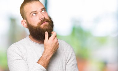 Genç Sarışın elle çene düşünme hakkında soru, dalgın ifade üzerine giyiyor rahat kazak adam. Düşünceli yüzüyle gülümsüyor. Şüphe kavramı.