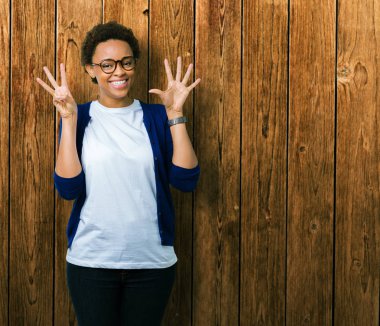 Genç güzel Afrikalı-Amerikalı kadın gözlük gösterilen ve parmakları ile işaret izole arka plan üzerinde kendinden emin ve mutlu gülümseyerek süre sekiz numara.