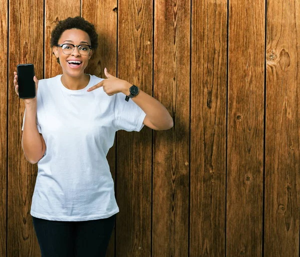 Young african american woman showing smartphone screen over isolated background with surprise face pointing finger to himself