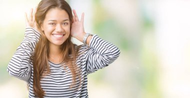 Her ikisi de dinliyoruz izole arka plan üzerinde çizgili süveter giyen genç güzel esmer kadın kulak jest, dedikodu için meraklı eller. İşitme sorunu, sağır