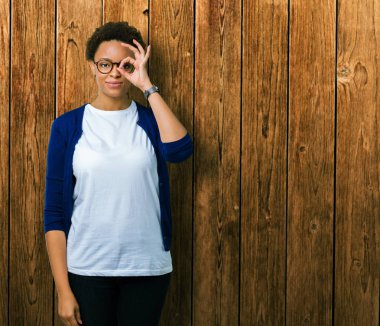 Genç güzel Afrikalı-Amerikalı kadın gülümsüyor, parmakları ile mutlu yüz üzerinden seyir göz el ile ok jest yapıyor izole arka plan üzerinde gözlük.