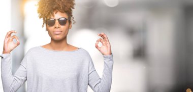 Güzel genç Afro-Amerikan kadın giyiyor güneş gözlüğü izole arka plan üzerinde dinlenmek ve gülümseyen gözlerle kapalı parmak jestle meditasyon yapıyor. Yoga kavramı.