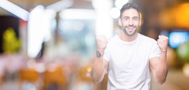 İzole arka plan kutlama üzerinde rahat beyaz t-shirt giyen genç adam şaşırttı ve silah ile başarı için yükseltilmiş ve açık gözler hayrete düşürdü. Kazanan kavramı.