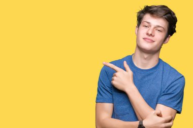 Yakışıklı delikanlı üzerinde izole mavi t-shirt giyen reklam, ciddi ve sakin yüz gösterilen yan el parmak ile işaret arka plan