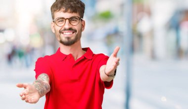 Sarılmak için kollarını açarak gülümseyerek kameraya bakarak izole arka plan üzerinde gözlük takan yakışıklı delikanlı. Neşeli ifade kucaklayan mutluluk.