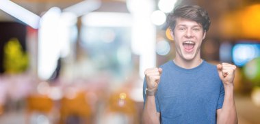 Yakışıklı delikanlı izole arka plan kutlama üzerinde mavi t-shirt giyen şaşırttı ve silah ile başarı için yükseltilmiş ve açık gözler hayrete düşürdü. Kazanan kavramı.