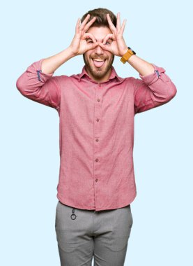 Genç yakışıklı iş casual adam dilini, parmaklarının arasından baktığını yapışmasını dürbün gibi ok jest yapıyor. Deli ifade.