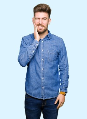 Diş ağrısı veya dişlerde dişlerle ilgili hastalık nedeniyle ağız acı ifadesi ile el ile dokunmak rahat kot gömlek giymiş genç yakışıklı sarışın adam. Diş hekimi kavramı.