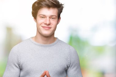 Arka plan eller üzerinde kış kazak giyen genç yakışıklı adam birlikte izole ve rahat ve neşeli gülümseyen parmak çarpı işareti. Başarı ve iyimser