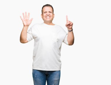 Orta yaş Arap adam wearig gösterilen ve parmakları ile işaret izole arka plan üzerinde beyaz t-shirt 6 gülümseyen ise kendinden emin ve mutlu numara.
