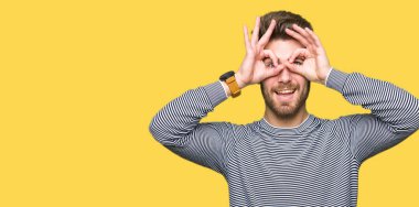 Çizgi kazak giyen genç yakışıklı adam dürbün yapışan gibi ok jest yapıyor, gözleri parmaklarla bakıyor. Çılgın ifade.