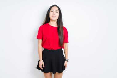 İzole arka planda kırmızı t-shirt ve etek giyen güzel esmer kadın yüzünde ciddi bir ifade ile rahat. Basit ve doğal kamera bakıyor.