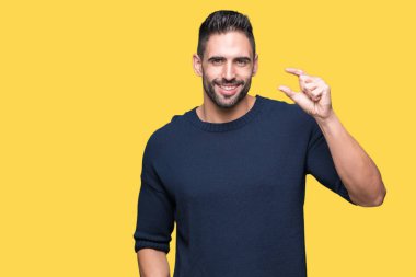 Genç yakışıklı adam üzerinde kazak giyiyor izole arka plan gülümseyen ve emin işaret ile el yapıyor boyutu işareti yaparken parmaklar ve kamera bakıyor. Ölçü kavramı.