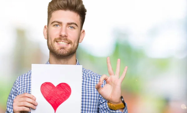 Jovem Homem Bonito Segurando Papel Com Coração Vermelho Fazendo Sinal — Fotografia de Stock