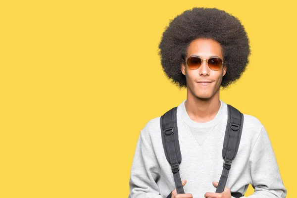 サングラスとバックパックを身に着けているアフロヘアの若いアフリカ系アメリカ人男性は 真剣に考えるスマートな顔に自信のある表情を持つ — ストック写真