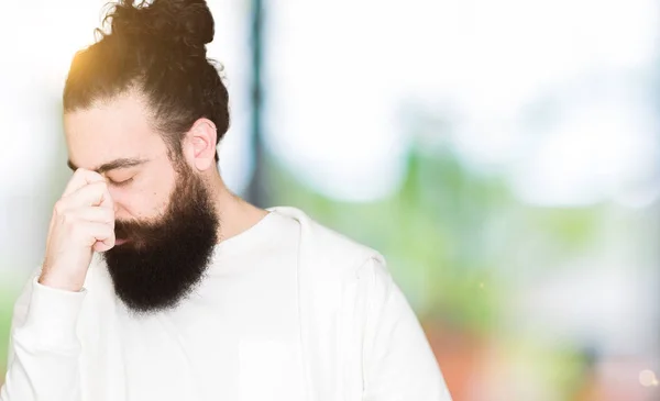 Young man with long hair and beard wearing sporty sweatshirt tired rubbing nose and eyes feeling fatigue and headache. Stress and frustration concept.