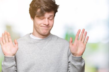 İzole arka plan clueless ve kollar ve elleri ile karıştı ifade üzerine sweatshirt giyen genç yakışıklı sportif adam kaldırdı. Şüphe kavramı.