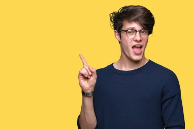 Kameraya bakarak yan el ve parmak ile işaret yüzünde kocaman bir gülümseme ile izole arka plan üzerinde gözlük takan genç yakışıklı adam.