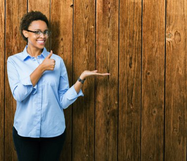 Genç güzel Afro-Amerikan iş kadını izole arka plan gösteren palm el ve yukarıya, mutlu ve neşeli gülümseyen baş parmakları Tamam jest yapıyor