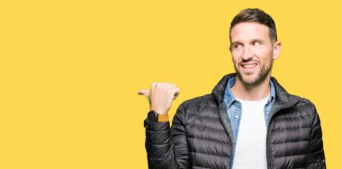 Yakışıklı adam arıyor ve başparmak yanında yukarıyı mutlu yüz ile gülümseyen kış palto giyiyor.