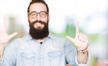 Uzun saç ve sakal gösterilen ve parmakları ile işaret gözlüklü genç hipster adam kendinden emin ve mutlu gülümseyerek süre yedi numara.