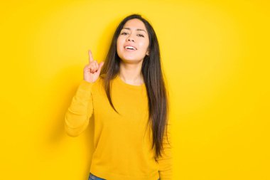 Başarılı bir fikir ile sarı izole arka plan işaret parmak üzerinde güzel esmer kadın. Çıktı ve mutlu. Bir numara.