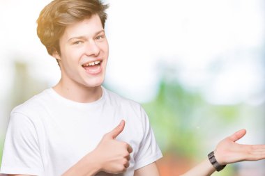 İzole arka plan gösteren palm el üzerinde rahat beyaz t-shirt giyen ve yukarıya, mutlu ve neşeli gülümseyen baş parmakları Tamam jest yapıyor yakışıklı delikanlı