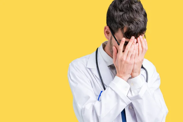 Young doctor man wearing hospital coat over isolated background with sad expression covering face with hands while crying. Depression concept.