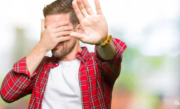 Handsome man wearing casual shirt covering eyes with hands and doing stop gesture with sad and fear expression. Embarrassed and negative concept.